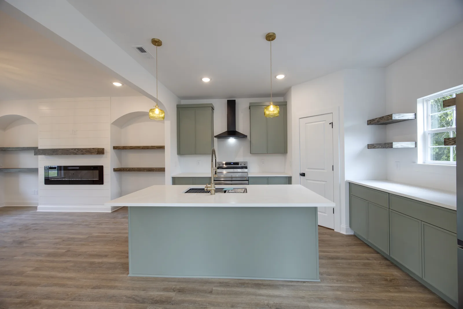 Kitchen with sage-green custom cabinetry, quartz counters, and floating oak shelves