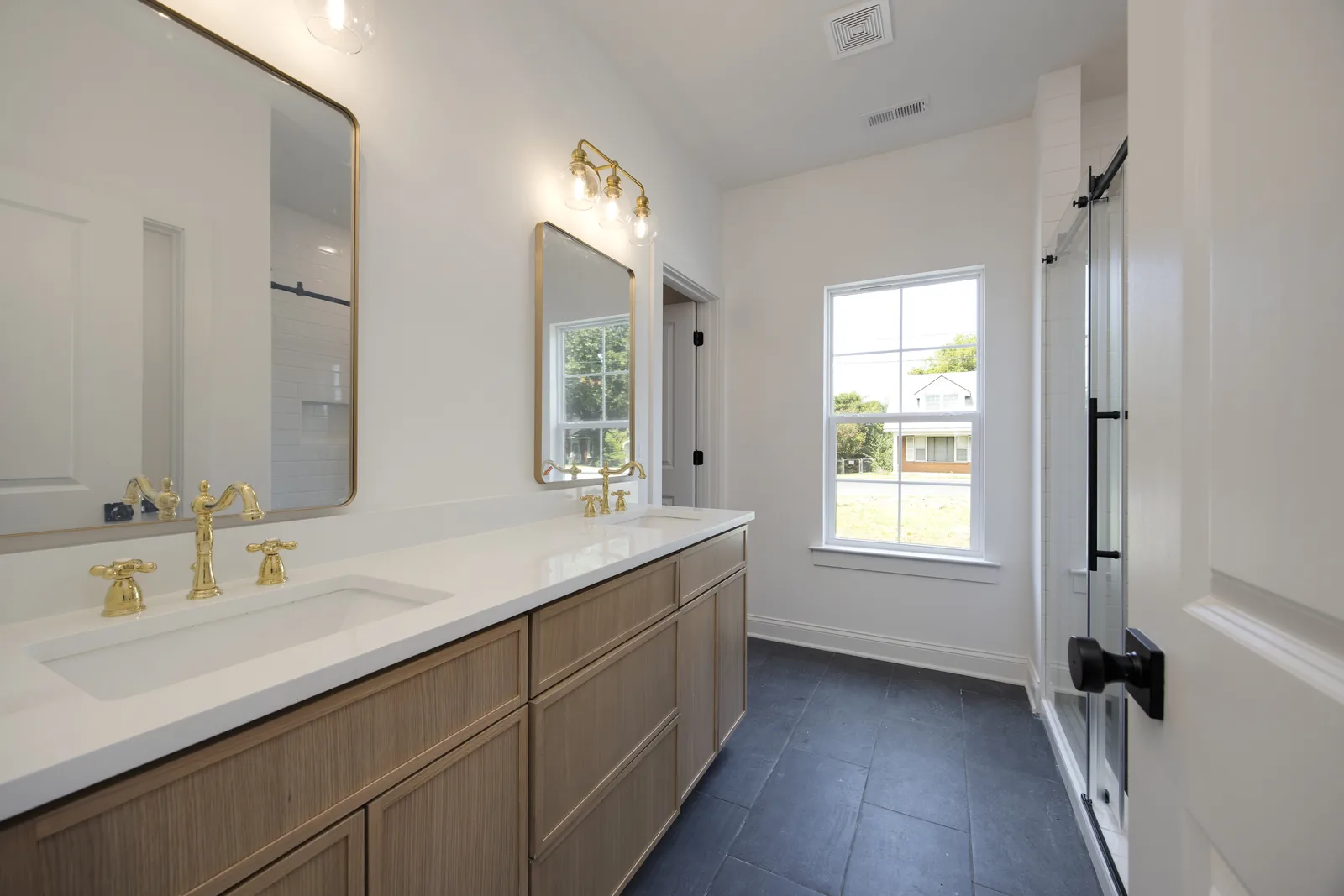 Double vanity with brass faucets and a sliding barn door to the bath