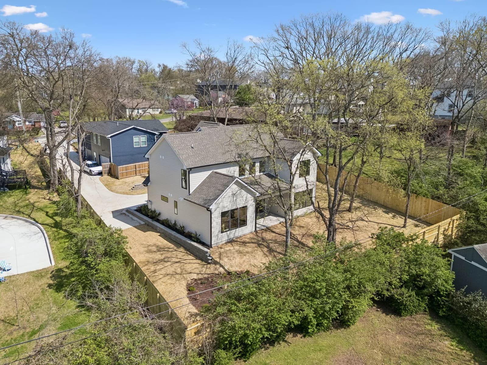 Aerial view of the home set among mature trees, fenced backyard behind