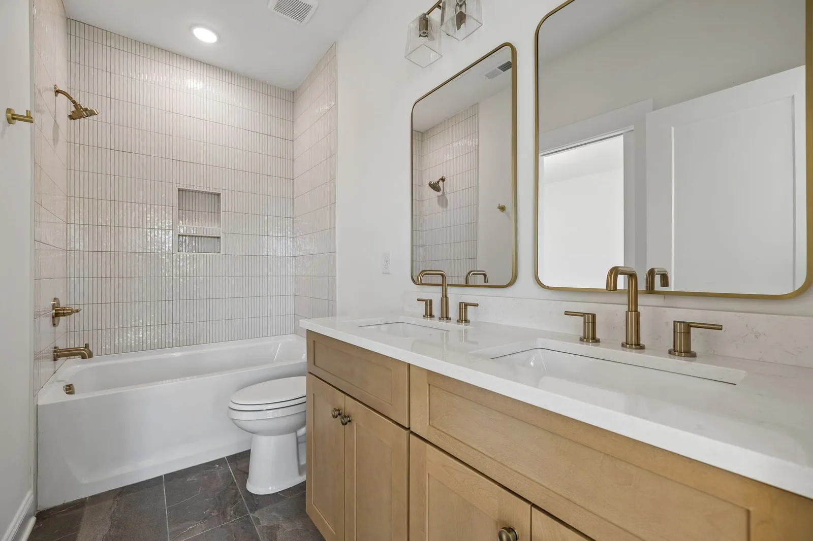 Bathroom with a tiled tub surround, brass fixtures, and a white-oak double vanity