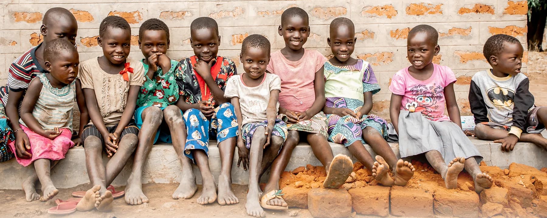 Ten children sitting together on the concrete stoop of their community's new brick home in Northern Uganda