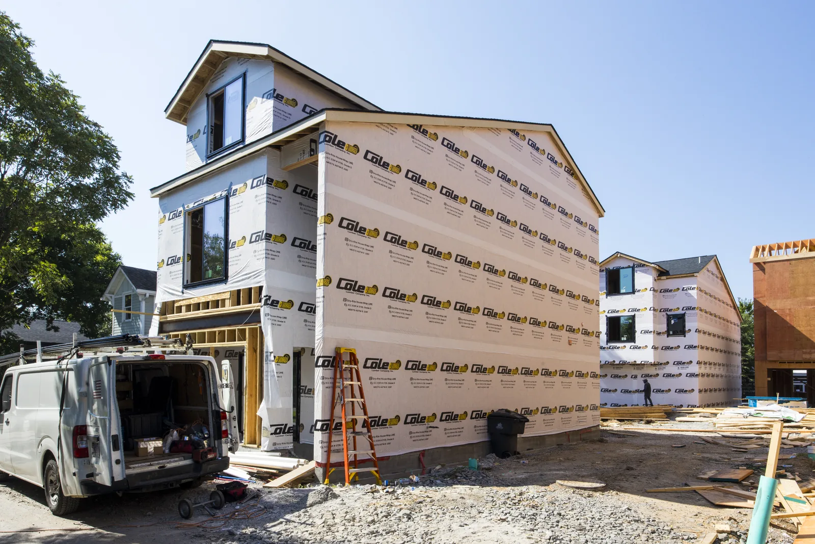Townhome at 909 Cheatham Pl wrapped in housewrap and nearing dry-in, windows set, with a work van and ladder on the gravel site
